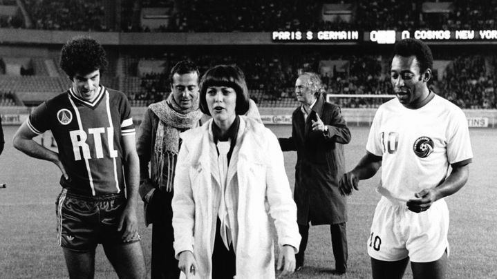 La chanteuse Mireille Mathieu s'apprêtant à donner le coup d'envoi du match PSG-Cosmos, entre Pelé et le joueur parisien Jacky Novi, le 14 septembre 1976, au Parc des Princes, à Paris. (PICOT / GAMMA-RAPHO)