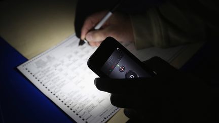 Un &eacute;lecteur d'Oceanside (New York)&nbsp;est contraint d'utiliser la lumi&egrave;re de son t&eacute;l&eacute;phone portable pour remplir son bulletin dans un bureau de vote touch&eacute; par l'ouragan Sandy. (BRUCE BENNETT / GETTY IMAGES / AFP)