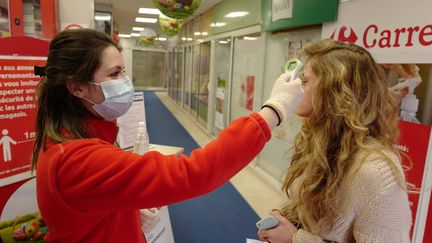 Une employée de supermarché prend la température d'une cliente à l'entrée du magasin, à Cannes (Alpes-Maritimes), le 8 avril 2020.&nbsp; (VALERY HACHE / AFP)