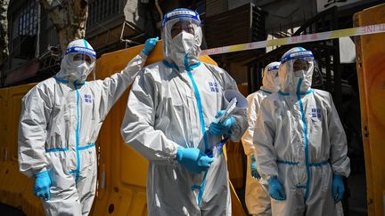 Des employés d'une organisation de service public portant des équipements de protection livrent des légumes aux habitants d'un quartier en confinement, dans le district de Jing'an, à Shanghai, le 29 mars 2022. (HECTOR RETAMAL / AFP)