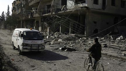 Une ambulance passe devant des bâtiments lourdement endommagés à Hammuriyeh dans la zone de la Ghouta orientale tenue par les rebelles, à la périphérie de la capitale Damas (Syrie), le 12 février 2016. (ABDULMONAM EASSA / AFP)