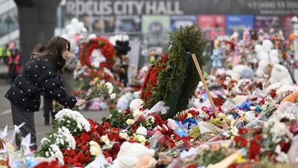 Une jeune femme dépose des fleurs, le 29 mars 2024, devant le Crocus City Hall, la salle de concert en banlieue de Moscou (Russie) visée par un attentat qui a fait plus de 140 morts. (NATALIA KOLESNIKOVA / AFP)