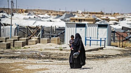 Une femme portant un enfant passe devant des tentes dans le camp de prisonniers jihadistes d'Al-Hol, situé dans le nord-est de la Syrie, le 11 mai 2021. (DELIL SOULEIMAN / AFP)