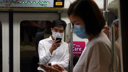 Des passagers du Mass Rapid Transit portent des masques faciaux comme mesure préventive contre le coronavirus Covid-19 à Singapour, le 18 mars 2020. (CATHERINE LAI / AFP)