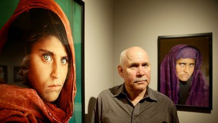 Steve McCurry posant à côté de son célèbre portrait de la jeune afghane Sharbat Gula.
 (Ulrich Perrey/DPA/AFP)