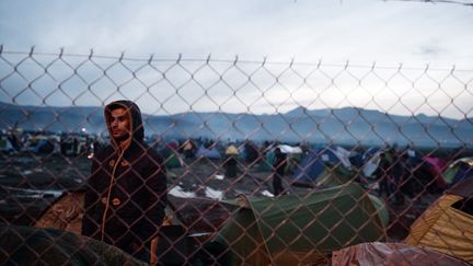 Le 8 mars 2016, un migrant regarde le grillage de barbelés qui le sépare de la frontière macédonienne. (LOUISA GOULIAMAKI / AFP)