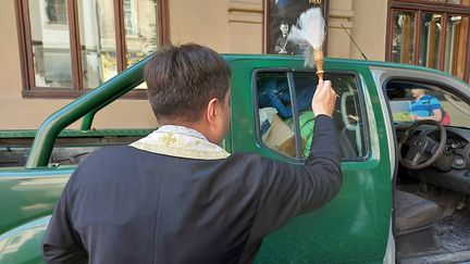 Le pope bénit une voiture, à Lviv, avant le départ du véhicule vers le Donbass. (Julie Pietri / Radio France)