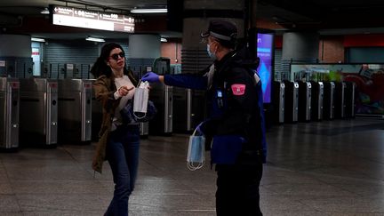 Un policier tend un masque à une passante à la gare d'Atocha, à Madrid (Espagne), le 13 avril 2020. (JAVIER SORIANO / AFP)