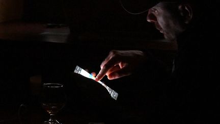 Le client d'un bar regardant son smartphone dans l'obscurité pendant une coupure de courant dans un bar de Kiev, le 24 octobre 2022. (SERGEI SUPINSKY / AFP)