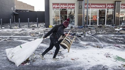 Un homme soupçonné d'être un pillard traîne un sac près d'un magasin vandalisé à&nbsp;Vosloorus, dans la banlieue de Johannesbourg, le 14 juillet 2021. (MARCO LONGARI / AFP)