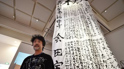 L'artiste Makoto Aida, l'un des artiste contemporain les plus connus au Japon pose à côté de son oeuvre controversée, une calligraphie géante qui critique ouvertement le ministère de l'Education dans une exposition dédiée aux enfants.
 (KAZUHIRO NOGI / AFP)