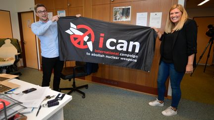 La dirigeante de l'Ican, Béatrice Fihn, et le coordinateur de l'organisation,&nbsp;Daniel Hogstan, brandissent une bannière de leur coalition, le 6 octobre 2017, à Genève (Suisse) pour fêter leur prix Nobel de la paix. (FABRICE COFFRINI / AFP)