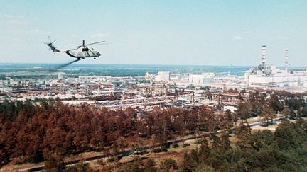 Un hélicoptère militaire&nbsp;diffuse un produit supposé réduire la contamination de l'air,&nbsp;au-dessus&nbsp;de la&nbsp;centrale&nbsp;nucléaire de Tchernobyl, à Prypiat, en URSS (aujourd'hui sur le territoire ukrainien), quelques jours après la catastrophe du 26 avril 1986. (STF / TASS / AFP)