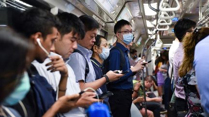 Des passagers du Mass Rapid Transit portent des masques faciaux comme mesure préventive contre le coronavirus Covid-19 à Singapour, le 18 mars 2020. (CATHERINE LAI / AFP)