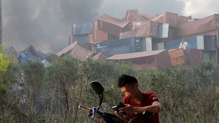 Ce Chinois de Tianjin consulte son portable tandis que,&nbsp;au second plan, des conteneurs renvers&eacute;s t&eacute;moignent de la violence du choc apr&egrave;s l'explosion du 12 ao&ucirc;t 2015. (REUTERS )