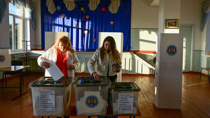 Deux personnes votent durant l'élection présidentielle et un référendum sur l'adhésion de la Moldavie à l'Union européenne dans un bureau de vote du village d'Hirbovat (Moldavie), le 20 octobre 2024. (DANIEL MIHAILESCU / AFP)