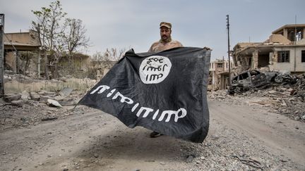 Un soldat de l'armée irakienne tient un drapeau du groupe Etat islamique, à Mossoul, le 7 juillet 2017. (NurPhoto/AFP)