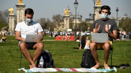 Deux hommes télétravaille sur la pelouse du parc des Invalides à Paris, le 31 mars 2021. (BERTRAND GUAY / AFP)