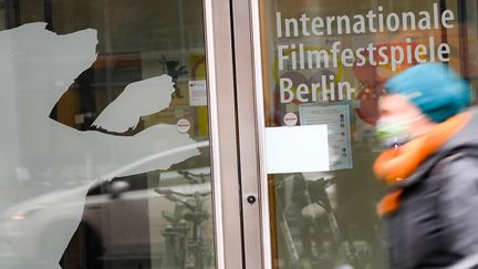 Une passante masquée devant l'entrée d'un bâtiment, Potsdamer Platz, où l'on peut lire "Festival international du film de Berlin" et voir la reproduction de la silhouette d'un ours, emblème de la Berlinale, le 11 décembre 2020 à Berlin. (JENS KALAENE / DPA / MaxPPP)