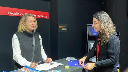 Émilie Nicolas (à gauche), responsable de l’École du livre de jeunesse, et Nasim Kiani, gestionnaire de formation, sur le stand de l'organisme au Salon du livre et de la presse jeunesse le 29 novembre à Montreuil (Seine-Saint-Denis). (FG/FRANCEINFO)