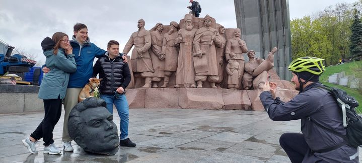 Des habitants de Kiev se photographient devant ce qu'il reste de la statue symbolisant l'amitié russo-ukrainienne après son démontage à Kiev, le 26 avril 2022. Au fond, une stèle en granit qui elle, reste en place. (FABIEN GOSSET / RADIO FRANCE)