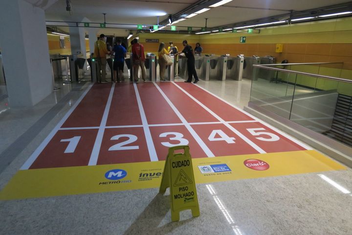 Une pancarte indique "attention, sol glissant", devant une fausse piste d'athlétisme disposée dans la ligne 4 du métro de Rio de Janeiro (Brésil), le 4 août 2016. (PIERRE GODON / FRANCETV INFO)