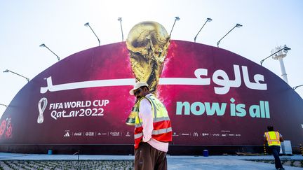 Des ouvriers marchent devant un panneau d'affichage de la Coupe du monde de football 2022 à Doha (Qatar), le 29 octobre 2022. (JEWEL SAMAD / AFP)
