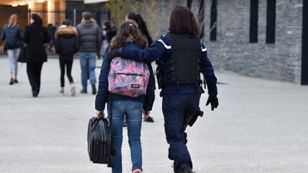 Une élève est accompagnée par une gendarme à son arrivée vendredi au collège Christian Bourquin, à Millas, où une cellule psychologique a été installée. (PASCAL PAVANI / AFP)