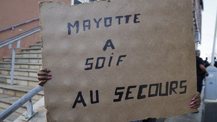 Un Mahorais brandit une pancarte "Mayotte a soif", le 19 décembre 2024, lors de la visite d'Emmanuel Macron sur l'archipel. L'accès à l'eau potable, déjà très difficile avant le passage du cyclone Chido, se complique depuis la catastrophe. (LUDOVIC MARIN / POOL)