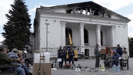 Des habitants rechargent leurs téléphones avec un générateur, devant le théâtre de Marioupol partiellement détruit, en mai 2022. (STRINGER / AFP)