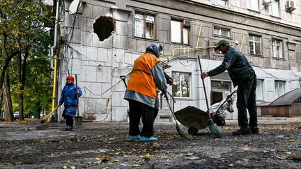 Des habitants nettoient les débris devant un immeuble détruit par une frappe des troupes russes, à Zaporijjia, dans le sud de l'Ukraine, le 21 octobre 2022.&nbsp; (DMYTRO SMOLIYENKO / NURPHOTO / AFP)