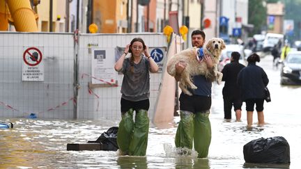 Des habitants portent leur chien dans une rue inondée de Lugo, en Italie, le 18 mai 2023. (ANDREAS SOLARO / AFP)