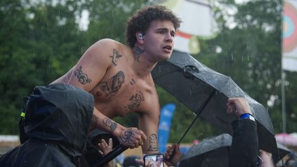 Le rappeur britannique Slowthaï torse nu dans la foule alors qu'il pleut à verse, capuche et parapluie en témoignent, dimanche 5 juin 2022 au festival We Love Green. (DAVID WOLFF - PATRICK / REDFERNS / GETTY)