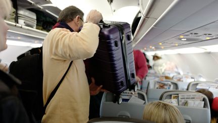 Un passager dépose son bagage cabine dans un avion à l'aéroport de Roissy - Charles de Gaulle, en mai 2023 (illustration). (ERIC BERACASSAT / AFP)