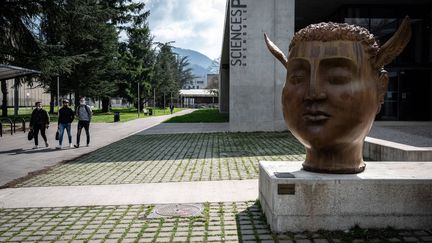 Des étudiants passent devant la statue "Hypnos" de l'artiste espagnol Jose Seguiri à l'entrée du campus de Sciences-Po Grenoble, à Saint-Martin-d'Heres, près de Grenoble, le 8 mars 2021. (JEAN-PHILIPPE KSIAZEK / AFP)