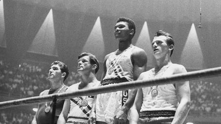 Les vainqueurs des médailles olympiques de 1960 en boxe mi-lourd sur le podium des vainqueurs à Rome : Cassius Clay (aujourd'hui Muhammad Ali) (au centre), or ; Zbigniew Pietrzykowski, de Pologne (à droite), argent ; et Giulio Saraudi (Italie) et Anthony Madigan (Australie), bronze ex aequo. (CENTRAL PRESS / HULTON ARCHIVE)