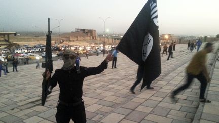 Un combattant de l'Etat islamique brandit une arme et un drapeau dans une rue de Mossoul (Irak) en juin 2014.&nbsp; (REUTERS)