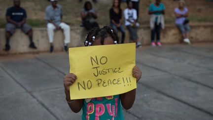 Une petite fille tient devant son visage une feuille avec l'inscription "pas de justice, pas de paix" . (NICHOLAS KAMM / AFP)