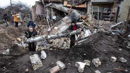 Deux hommes ramassent des débris dans un village bombardé près de Kiev (Ukraine), le 31 décembre 2022. (OLEKSII CHUMACHENKO / ANADOLU AGENCY / AFP)