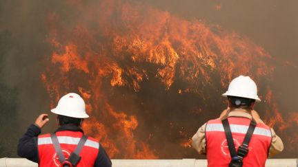 Deux pompiers observent les flammes qui ont détruit une centaine de maisons. (RODRIGO GARRIDO / REUTERS)