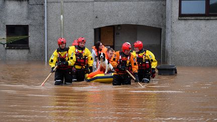 Un couple et leur chien sont secourus par une équipe des garde-côtes d'une rue inondée à Brechin, dans le nord-est de l'Ecosse, le 20 octobre 2023, alors que la tempête Babet frappe le pays. (ANDY BUCHANAN / AFP)