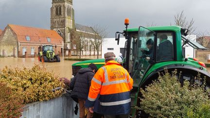 Frédéric Dumont prend des passagers à bord de son tracteur, le 3 janvier 2024 à Thérouanne (Pas-de-Calais), alors que la place de la salle communale est totalement sous les eaux. (FABIEN MAGNENOU / FRANCEINFO)