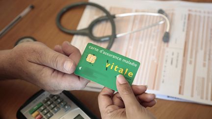 Un patient et un médecin&nbsp;échangent une carte vitale lors d'une consultation. En France, le reste à charge pour les ménages est l'un des plus faibles de l'OCDE avec seulement 2% de frais. (VINCENT ISORE / MAXPPP)