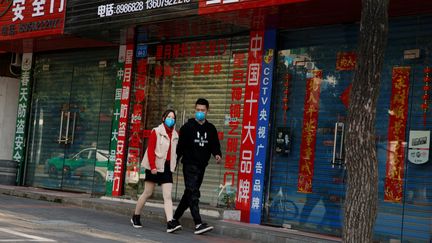 Des passants marchent devant les rideaux baissés de magasins fermés à cause de l'épidémie de coronavirus, le 4 février 2020 à Jiujiang (Chine). (THOMAS PETER / REUTERS)