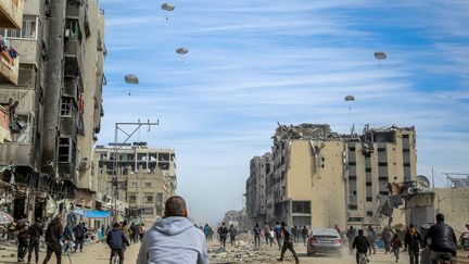 Des Palestiniens courent alors que l'aide humanitaire est larguée par avion dans la ville de Gaza, le 1er mars 2024. (- / AFP)