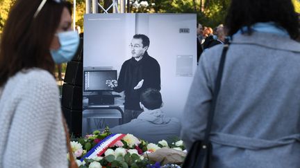 Des personnes venues rendre hommage à Samuel Paty se tiennent devant une photographie du professeur, lors d'une cérémonie organisée à&nbsp;Eragny-sur-Oise dans le Val-d'Oise le 16 octobre 2021. (ALAIN JOCARD / AFP)