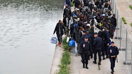 Des policiers anti-émeutes escortent des migrants et des réfugiés lors de l'évacuation du camp de fortune du "Millenaire" le long du Canal de Saint-Denis près de la Porte de la Villette, au nord de Paris, le 30 mai 2018. (GERARD JULIEN / AFP)