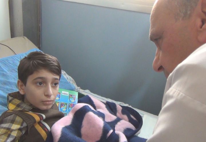 Le docteur Hadid réconforte le jeune Abdel grièvement blessé à la jambe gauche par un obus à Alep, en Syrie.&nbsp; (GILLES GALLINARO / RADIO FRANCE)