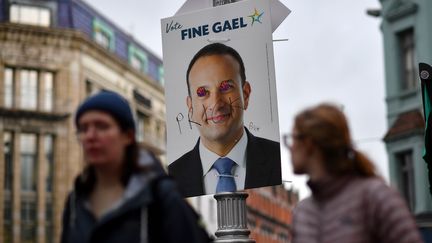 Des piétons passent devant une affiche électorale taguée représentant le Premier ministre irlandais Leo Varadkar, vendredi 7 février 2020 à Dublin. (BEN STANSALL / AFP)