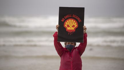 Cette femme manifeste contre le projet de la compagnie pétrolière Shell de mener des études sismiques sous-marines le long de la côte Est de l'Afrique du Sud, la fameuse "Wild Coast", à Muizenberg Beach, au Cap, le 5 décembre 2021. (RODGER BOSCH / AFP)